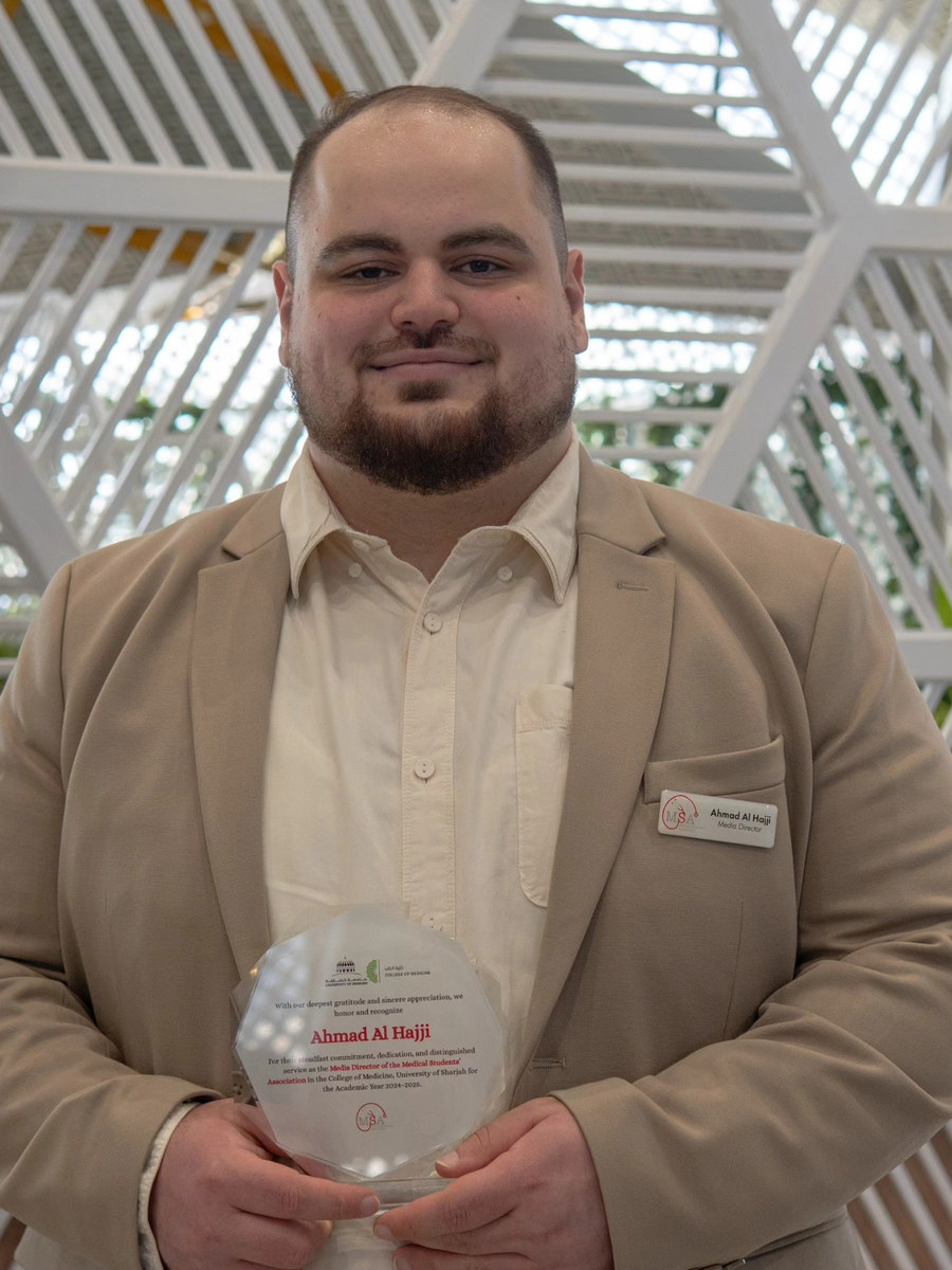 Ahmad Al Hajji in a beige blazer, holding a recognition plaque
